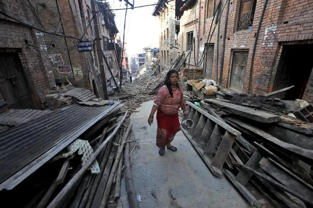 A Nepalese woman carrying utensils walks past damaged houses in Bhaktapur, Nepal, Thursday, May 14, 2015. The past three weeks have been misery for Nepal. On April 25, a magnitude-7.8 earthquake killed thousands of people, injured tens of thousands more and left hundreds of thousands homeless. Then, just as the country was beginning to rebuild, a magnitude-7.3 earthquake battered it again. (AP Photo/Bikram Rai)