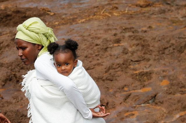 A woman carries her child near the scene of search and rescue operations after heavy flash floods wiped out several homes when a dam burst, following heavy rains in Kamuchiri village of Mai Mahiu, Nakuru County, Kenya on April 29, 2024. (Photo by Thomas Mukoya/Reuters)