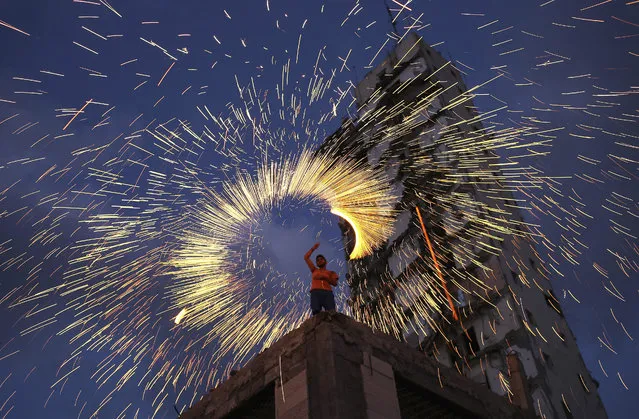 A picture made available on 29 June 2015 shows a Palestinian lighting fireworks amid the rubble of an Italian tower in Gaza City, Gaza Strip, 27 June 2015. A group of Palestinians put their aims to light the darkness with fireworks at devastated urban areas in the Gaza Strip during the holy month of Ramadan. The group's intent is to give hope to the people who lost their houses during the Israel-Gaza conflict in 2014. (Photo by Mohammed Saber/EPA)