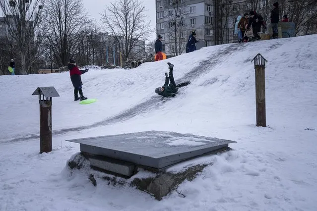 A boy slides down an ice slide in Kharkiv, Ukraine, Sunday, January 30, 2022. (Photo by Evgeniy Maloletka/AP Photo)
