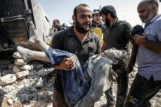 A Syrian carries the body of a child at the site of a reported regime air strike on the village of Deir Sharqi on the eastern outskirts of Maaret al-Numan in Syria's northern province of Idlib on August 17, 2019. Regime air strikes killed one woman and six of her children in northwest Syria, a war monitor said, a day after Russian bombardment pummelled a nearby displacement camp. (Photo by Abdullah Hammam/AFP Photo)
