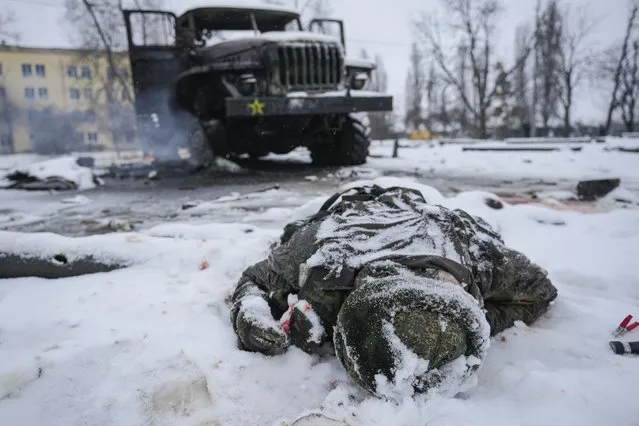 The body of a serviceman is coated in snow next to a destroyed Russian military multiple rocket launcher vehicle on the outskirts of Kharkiv, Ukraine, Friday, February 25, 2022. Russian troops bore down on Ukraine's capital Friday, with gunfire and explosions resonating ever closer to the government quarter, in an invasion of a democratic country that has fueled fears of wider war in Europe and triggered worldwide efforts to make Russia stop. (Photo by Vadim Ghirda/AP Photo)