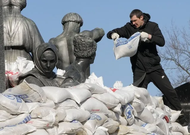 A city resident covers the monument to Taras Shevchenko, a famous Ukrainian poet and a national symbol, with sandbags to protect from the Russian shelling, in Kharkiv, Ukraine, Thursday, March 24, 2022. The bronze 16 meter high monument was opened in 1935, survived WWII and is considered one of the world's best monuments to Shevchenko. (Photo by Efrem Lukatsky/AP Photo)