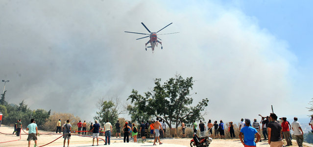 An helicopter operates over the crowd on the mountain of Ymittos in Athens, Friday, July 17, 2015. (Photo by Giannis Kotsiaris/InTime News via AP Photo)