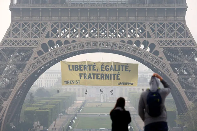 Tourists walk at Trocadero square as activists from the environmentalist group Greenpeace unfurl a giant banner on the Eiffel Tower which reads “Liberty, Equality, Fraternity” in a call on French citizens to vote against the National Front (FN) presidential candidate Marine Le Pen, in Paris, France May 5, 2017. (Photo by Gonzalo Fuentes/Reuters)