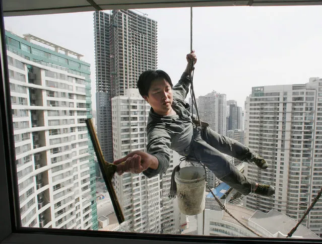 A worker cleans the windows of an apartment block in Beijing's central business district April 4, 2007. (Photo by Reinhard Krause/Reuters)