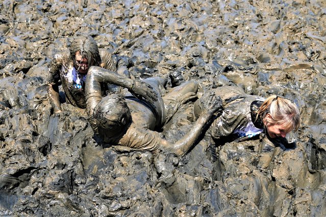 Competitors take part in the annual Maldon Mud Race, a charity event to race across the bed of the River Blackwater in Maldon, Essex on Sunday, May 14, 2023. The race originated in 1973, with a dare being given by a local resident to the landlord of the Queens Head public house, which stands on the Hythe Quay in Maldon, challenging him to serve a meal on the saltings of the Rivers Blackwater dressed in a dinner jacket. The challenge was accepted and carried out, resulting next year in a bar being opened on the saltings. About twenty people made a mad dash across the river bed, drank a pint of beer and dashed back. (Photo by Joe Giddens/PA Wire)