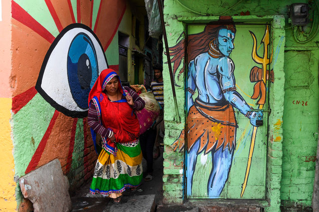 A woman walks out of an alleyway adorned with murals painted by artists from “Delhi Street Art” group at the Raghubir Nagar slum in New Delhi on December 2, 2019. A New Delhi slum has been given a colourful makeover thanks to a street artist collective, drawing art lovers and selfie-snappers to a rundown area that they would never normally visit. (Photo by Sajjad Hussain/AFP Photo)