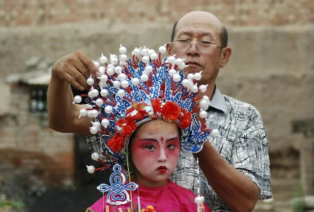 A craftsman (back) adjusts the headwear on a young girl for a local folk performance, on the outskirts of Hohhot, Inner Mongolia Autonomous Region, June 29, 2014. (Photo by Reuters/Stringer)