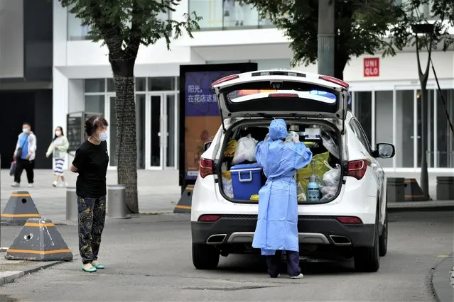 A woman wearing a face mask looks at a medical worker in protective gear preparing to collect coronavirus test samples at a closed shopping mall as part of COVID-19 controls in Beijing, Monday, June 13, 2022. (Photo by Andy Wong/AP Photo)