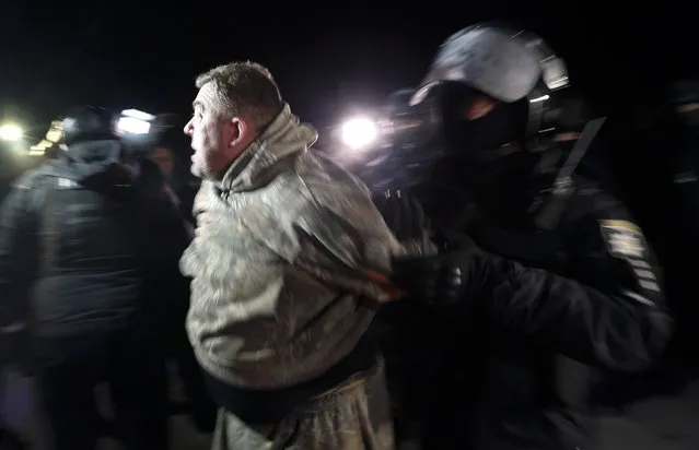 A Ukrainian riot police officer detains a protester, who planned to stop buses carrying passengers evacuated from the Chinese city of Wuhan, outside Novi Sarzhany, Ukraine, Thursday, February 20, 2020. Several hundred residents in Ukraine's Poltava region protested to stop officials from quarantining the evacuees in their village because they feared becoming infected. Demonstrators put up road blocks and burned tires, while Ukrainian media reported that there were clashes with police, and more than 10 people were detained. (Photo by Efrem Lukatsky/AP Photo)