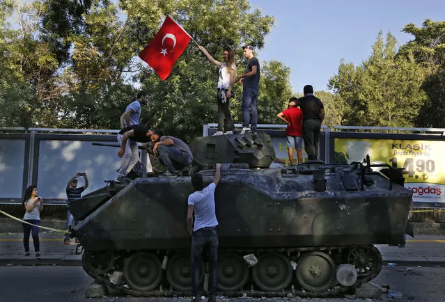 Turkish citizens stand on a damaged Turkish military APC that was attacked by protesters in a street near the Turkish military headquarters in Ankara, Turkey, Saturday, July 16, 2016. (Photo by Hussein Malla/AP Photo)