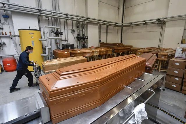 A worker takes in a coffin in the Crematorium Temple of Piacenza, Northern Italy, saturated with corpses awaiting cremation due to the coronavirus emergency Monday, March 23, 2020. (Photo by Claudio Furlan/LaPresse via AP Photo)
