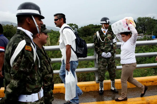 A young woman carries toilet paper as she crosses the Colombian-Venezuelan border over the Simon Bolivar international bridge after shopping while a Colombian police officer looks on in Cucuta, Colombia, July 16, 2016. (Photo by Carlos Eduardo Ramirez/Reuters)