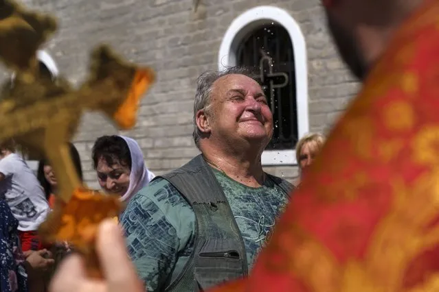 Archpriest Oleksandr Kondratyuk, right, blesses a congregant with holy water outside St. Michael's Ukrainian Orthodox Church of the Moscow Patriarchate for Savior of the Honey Feast Day in Pokrovsk, Donetsk region, eastern Ukraine, Sunday, August 14, 2022. (Photo by David Goldman/AP Photo)