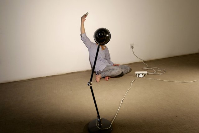 Chinese artist Zhou Jie holds up her cellphone to get a stronger signal as she tries to upload a picture at the Beijing Art Now Gallery, on August 19, 2014. As part of an art project, Zhou is living inside an exhibition hall with an unfinished iron wire bed, some iron wire sculptures in the shape of stuffed animals, an allotment of food and her mobile phone for 36 days. She began on August 9, 2014. (Photo by Jason Lee/Reuters)