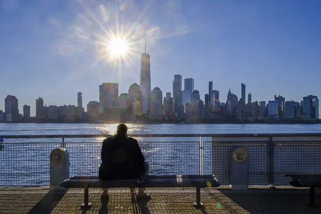 A morning commuter sits on a bench at the ferry terminal in Jersey City, N.J. looking at the lower Manhattan skyline on a cloudless day in New York City, Thursday, August 18, 2022. (Photo by J. David Ake/AP Photo)