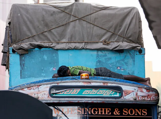 A man sleeps on top of a truck cabin parked along a road near a market in Colombo, Sri Lanka, July 22, 2016. (Photo by Dinuka Liyanawatte/Reuters)
