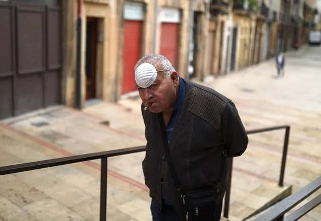 A man wearing a face mask on his forehead smokes a cigar while he walks outside, as some Spanish provinces are allowed to ease lockdown restrictions during phase one, amid the coronavirus disease (COVID-19) outbreak, in Tarragona, Spain, May 12, 2020. (Photo by Nacho Doce/Reuters)