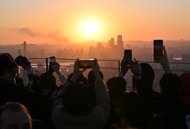 People take pictures as they observe the last sunset of the year on a viewing deck at Namsan tower in Seoul on December 31, 2024. (Photo by Jung Yeon-je/AFP Photo)