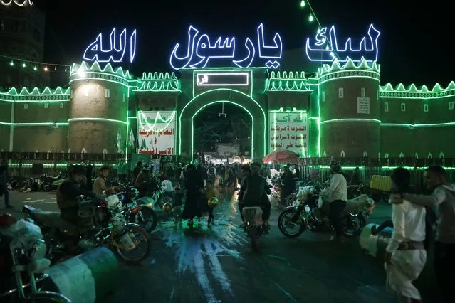 People walk through the main gate of the old city of Sana’a illuminated with green colorful lights and decorated with neon words reading in Arabic “At thy service, O Allah's Apostle” in preparation for celebrations of the birthday of the prophet Muhammad, in Sana'a, Yemen, 04 October 2022. (Photo by Yahya Arhab/EPA/EFE)