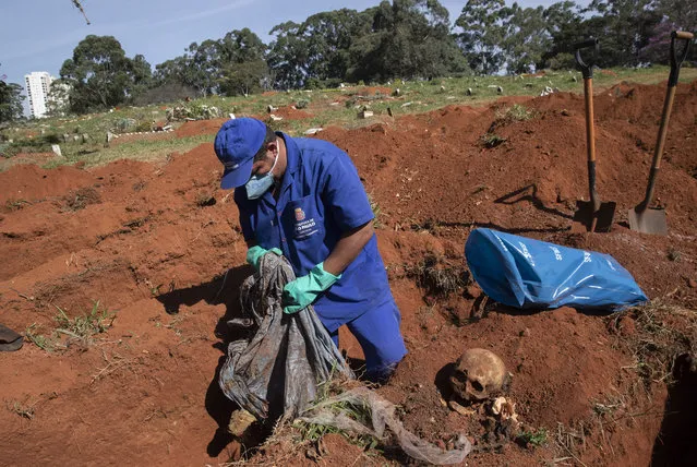 A cemetery worker exhumes the body of a person buried three years ago at the Vila Formosa cemetery, which does not charge families for the gravesites, in Sao Paulo, Brazil, Friday, June 12, 2020. Three years after burials, remains are routinely exhumated and stored in plastic bags to make room for more burials, which have increased amid the new coronavirus. (Photo by Andre Penner/AP Photo)