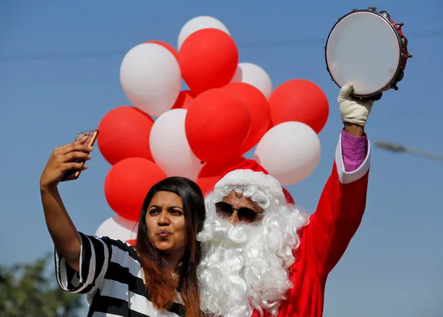 A woman takes a selfie with a man dressed as Santa Claus during a parade as part of Christmas celebrations in Ahmedabad, India, December 23, 2017. (Photo by Amit Dave/Reuters)