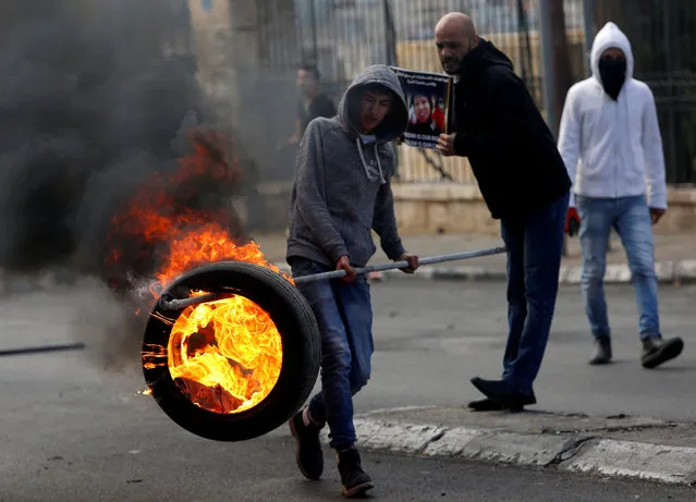 A Palestinian demonstrator moves a burning tire during clashes with Israeli troops, in the West Bank city of Bethlehem December 27, 2017. (Photo by Mussa Qawasma/Reuters)