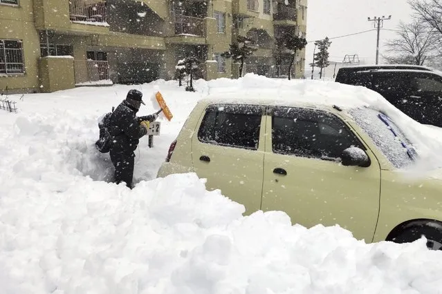 A resident shovels snow off around a car at a parking lot in Kitami city Hokkaido prefecture, northern Japan, on December 24 2022. (Photo by Kyodo News via AP Photo)