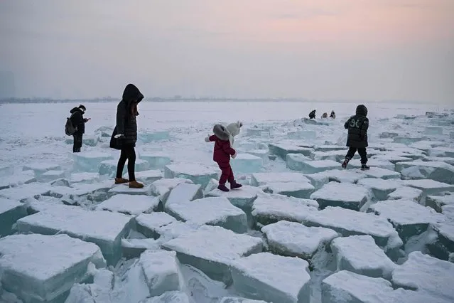 People walk on blocks of ice on the frozen Songhua river in Harbin, in China's northeastern Heilongjiang province, on January 6, 2023. (Photo by Hector Retamal/AFP Photo)