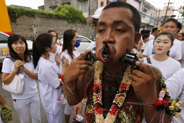 A devotee of the Chinese Bang Neow shrine walks with guns pierced through his cheeks during a procession celebrating the annual vegetarian festival in Phuket, Thailand October 18, 2015. (Photo by Jorge Silva/Reuters)