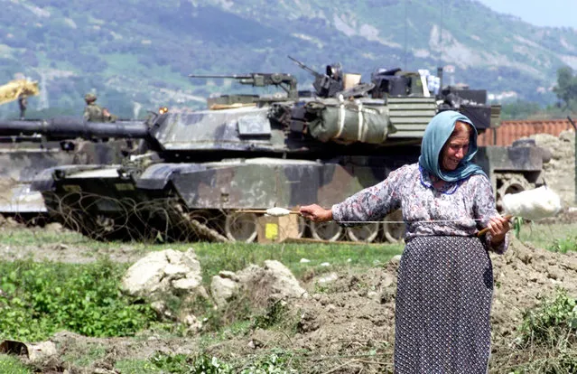 An Albanian woman spins wool in front of a US M1 Abrams tank, outside Tirana airbase Rinas, Wednesday, May 12, 1999. Rinas airbase plays crucial role in NATO's humanitarian mission “Shining Hope” as well as a base for possible military action. (Photo by Darko Bandic/AFP Photo)