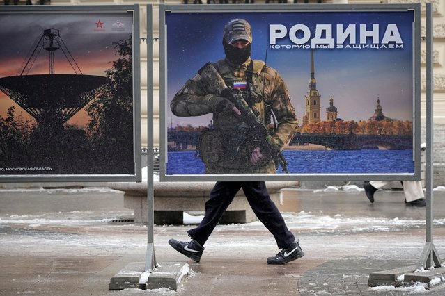 A man walks past a stand with an image of a Russian serviceman and words “The Motherland we defend” at a street exhibition of military photos in St. Petersburg, Russia, Monday, February 20, 2023. (Photo by Dmitri Lovetsky/AP Photo)
