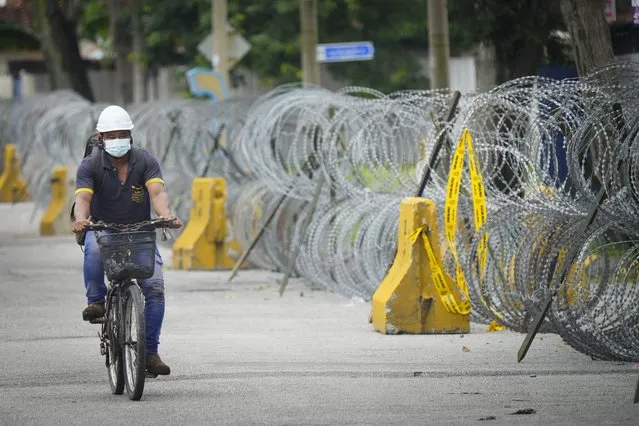 A men cycling next to coils of barbed wire near Top Glove factory hostel in Shah Alam, Malaysia, Wednesday, November 25, 2020. Malaysia's Top Glove Corp., the world's largest maker of rubber gloves, says it expects a two to four-week delay in deliveries after more than 2,000 workers at its factories were infected by the coronavirus, raising the possibility of supply disruptions during the pandemic. (Photo by Vincent Thian/AP Photo)