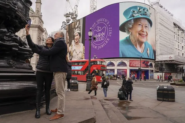 A couple take a selfie against the backdrop of the screen in Piccadilly Circus which is lit to celebrate the 70th anniversary of Britain's Queen Elizabeth's accession to the throne, in London, Sunday, February 6, 2022. (Photo by Alberto Pezzali/AP Photo)