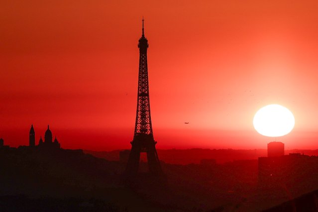 The sun rises by the Eiffel Tower and the Sacre Coeur Basilica ontop of the Montmartre hill in Paris on July 1, 2025, as the city is on red alert for high temperatures, with the top of the Eiffel Tower shut, polluting traffic banned and speed restrictions in place as a searing heatwave gripped Europe. Scientists say human-induced climate change is making such heatwave events more intense, frequent and widespread. Temperatures in France were expected to hit a peak today, according to the Meteo France weather agency, with the highest extreme heat warning in place in 16 departments across the country. (Photo by Thibaud Moritz/AFP Photo)