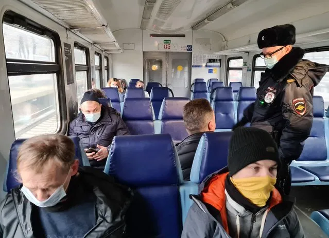 A Russian police officer checks public adherence of the 'mask regime' forcing people to wear masks in public places, in an electric train car in Moscow, Russia, Friday, November 27, 2020. Russia has registered a sharp spike in coronavirus cases Friday, with officials reporting 27,543 new confirmed infections, which is over 2,000 contagions more than the day before and the highest in the pandemic. (Photo by Denis Voronin, Moscow News Agency photo via AP Photo)