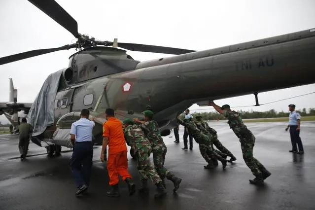 Military personnel move an Indonesian military helicopter used in recovery efforts for the missing AirAsia plane, as it sits idle due to bad weather, on the tarmac of Iskandar Airport in Pangkalan Bun, Central Kalimantan, December 31, 2014. (Photo by Darren Whiteside/Reuters)