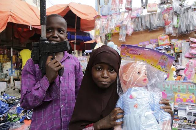 A Somali boy holds a toy gun as her sister holds a doll at a street market in Mogadishu, Somalia, Wednesday, April 19, 2023, as preparations are made for the Muslim holiday of Eid al-Fitr, next Friday, which marks the end of the holy fasting month of Ramadan. (Photo by Farah Abdi Warsameh/AP Photo)