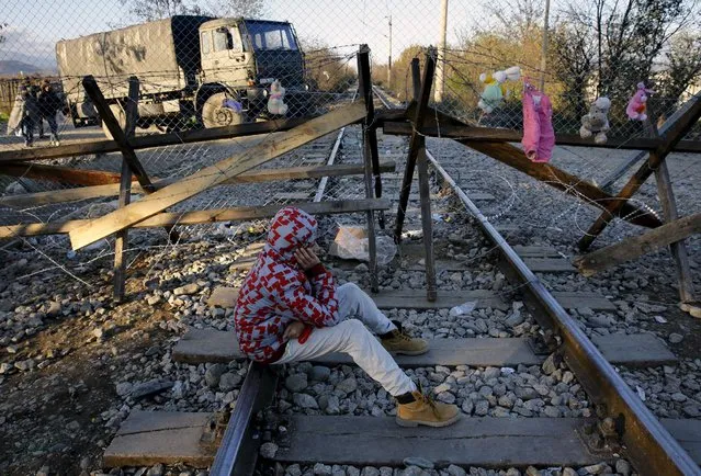Efran, 12, a stranded Iranian migrant sits on rail tracks in front of part of a fence erected on Sunda at the Greek-Macedonian border near the Greek village of Idomeni November 29, 2015. (Photo by Yannis Behrakis/Reuters)