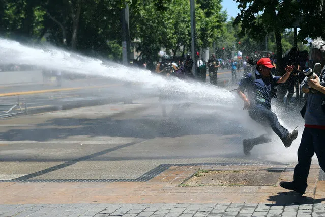 A demonstrator is hit by a jet of water released from a riot police vehicle as they clash during a strike against the national pension system in Santiago, Chile, November 4, 2016. (Photo by Ivan Alvarado/Reuters)