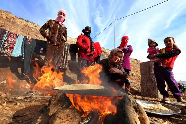 Displaced Iraqis from the Yazidi community, who fled violence between Islamic State (IS) group jihadists and Peshmerga fighters in the northern Iraqi town of Sinjar, wait for bread to bake at Dawodiya camp for internally displaced people in the Kurdish city of Dohuk, in Iraq's northern autonomous Kurdistan region, on January 14, 2015. (Photo by Safin Hamed/AFP Photo)