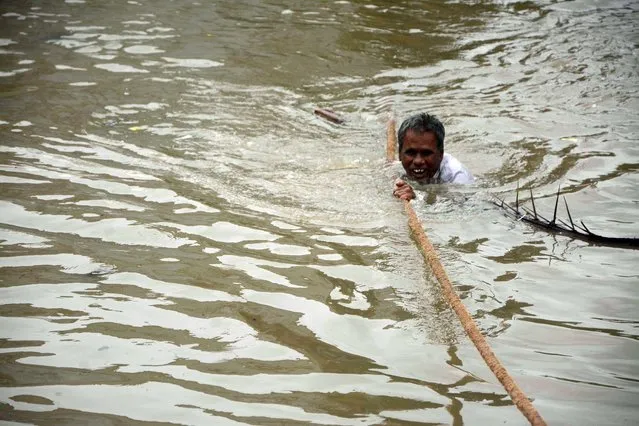 An Indian man clings to a rope as he makes his way through floodwaters in Chennai on December 2, 2015.   India has deployed troops to Tamil Nadu and closed the main airport there after heavy rains worsened weeks of flooding that has killed nearly 200 people in the southern coastal state. Thousands of rescuers carrying diving equipment, inflatable boats and medical equipment were battling to evacuate victims across the flooded state, officials said. (Photo by AFP Photo/Stringer)