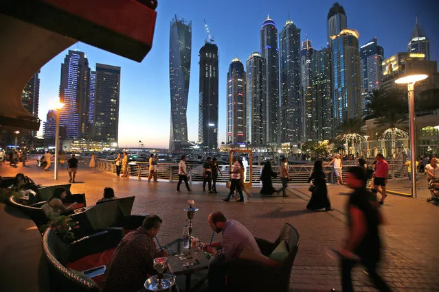 In this May 1, 2015 photo, two men play backgammon while smoking a shisha, or water pipe, at a restaurant overlooking the canal and the Marina neighborhood. Surrounding Marina's canal is an oasis of trendy restaurants and bars that serve an array of fusion-style cuisines that reflect the myriad of cultures and people drawn to Dubai, a modern city-state in the United Arab Emirates where foreigners far outnumber the locals. (Photo by Kamran Jebreili/AP Photo)