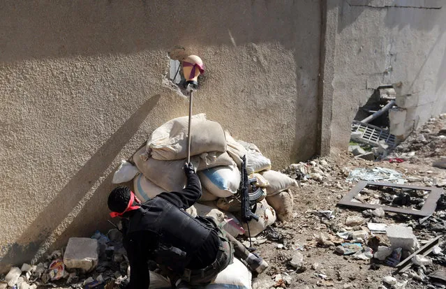 A “Free Syrian Army” fighter holds the head of a mannequin up to a hole in a wall of a Syrian Army base to attract and locate a sniper during heavy fighting in the Arabeen neighborhood of Damascus, on February 3, 2013. (Photo by Goran Tomasevic/Reuters)