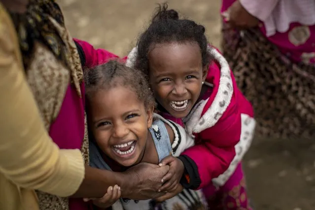 Two displaced Tigrayan girls giggle next to their mother, left, as their photograph is taken outside the Hadnet General Secondary School which has become a makeshift home to thousands displaced by the conflict, in Mekele, in the Tigray region of northern Ethiopia Wednesday, May 5, 2021. The Tigray conflict has displaced more than 1 million people, the International Organization for Migration reported in April, and the numbers continue to rise. (Photo by Ben Curtis/AP Photo)