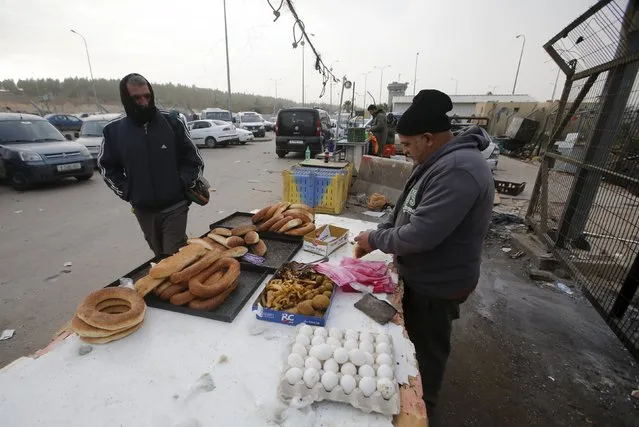 A Palestinian working in Israel buys food from a vendor as he waits to cross through the Israeli-controlled Mitar checkpoint south of the West Bank city of Hebron January 19, 2016. (Photo by Mussa Qawasma/Reuters)
