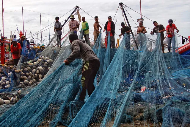 Fishermen gather to repair their nets as high waves prevent them from going out to sea at a fishing village in Lhokseumawe, Aceh on May 28, 2021. (Photo by Azwar Ipank/AFP Photo)