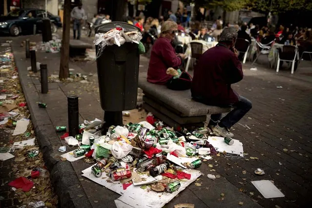 A couple sit on a public bench as garbage spills out of a full trash can during the sixth day of a garbage collectors strike in Madrid, on November 10, 2013. Street cleaners and garbage collectors who work in the city's public parks walked off the job in a strike called by trade unions to contest the planned layoff of more than 1,000 workers. Madrid's municipal cleaning companies, which have service supply contracts with the city authorities, employ some 6,000 staff. (Photo by Daniel Ochoa de Olza/Associated Press)