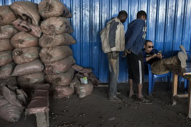 A Chinese “comptoir”, or counter, seated, calculates a payment as “creuseurs”, or diggers eagerly look on at Musompo, a mineral market outside Kolwezi on June 7, 2016. The cobalt dug up by the diggers is sold to Congo Dongfang International Mining(CDM). Cobalt is used in batteries for electronic cars and mobile phones and the DRC has roughly 65 percent of the world's supply. Workers and Congolese government officials claim that scales and metal analyzers are rigged and humidity content exaggerated in an effort to secure lower prices from diggers. Child labor, unsafe working conditions and contamination are all evident in the cobalt mining process. (Photo by Michael Robinson Chavez/The Washington Post)